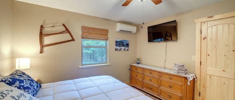 Una camera da letto con un letto, una cassettiera in legno, una ventola a soffitto, una finestra con persiane e un televisore fissato al muro.
