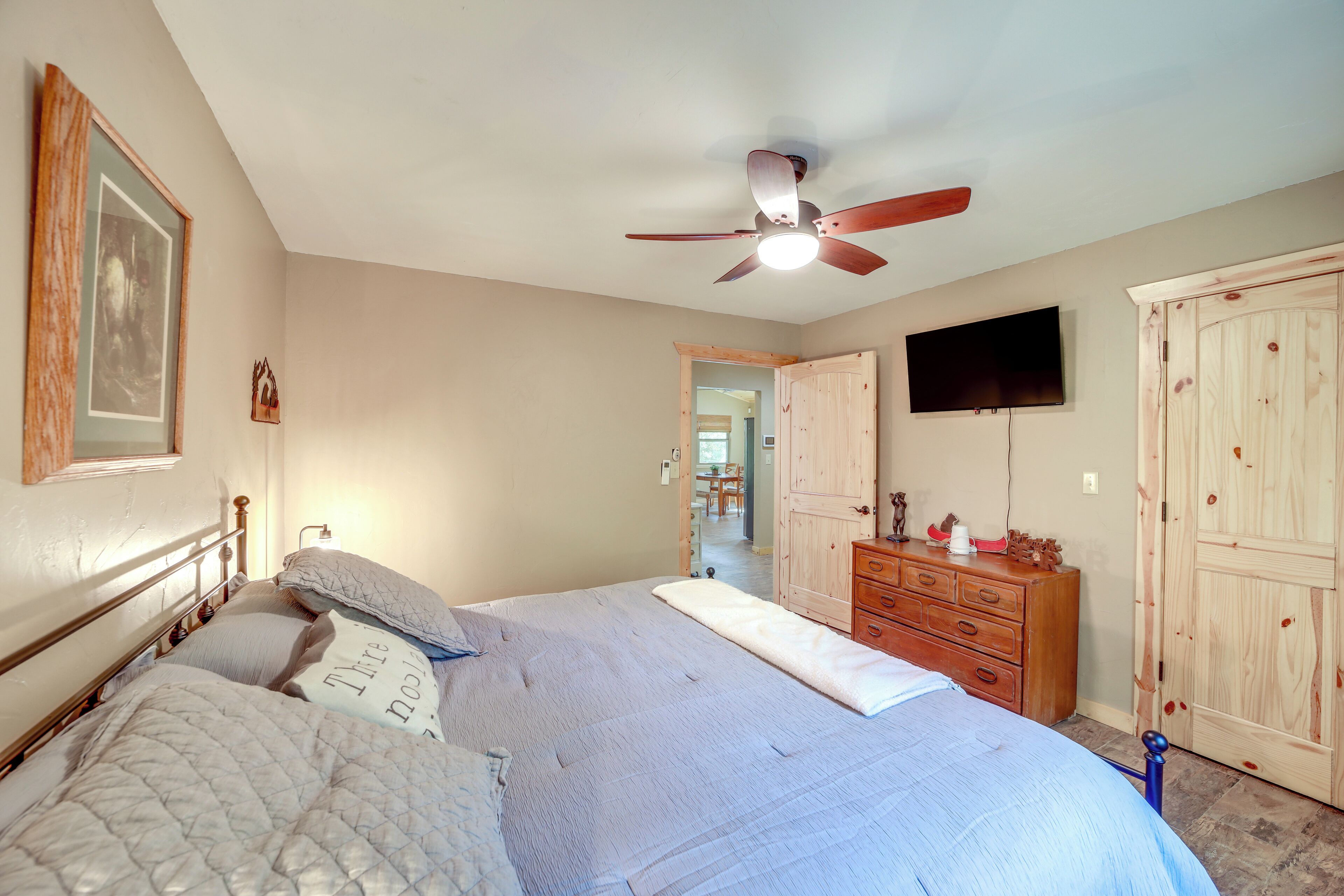 A bedroom with a bed, a ceiling fan, a dresser, and a television on the wall.