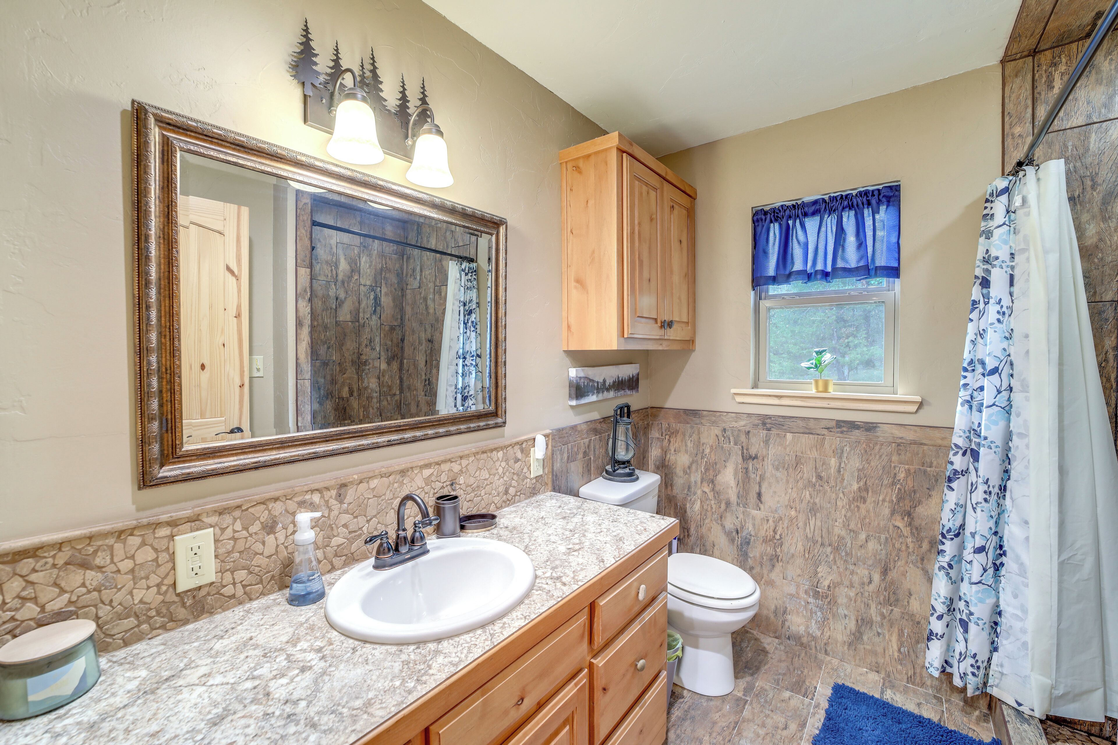 A bathroom with a granite countertop sink, wooden cabinets, a large mirror, a toilet, and a shower curtain.