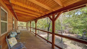 A covered wooden deck with benches and a railing, overlooking a wooded area. - Clayton Cabin w/ Wraparound Deck: Steps to Lake! (Clayton)