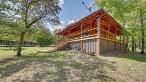 A wooden cabin with a covered porch, large windows, and a satellite dish. - Clayton Cabin w/ Wraparound Deck: Steps to Lake! (Clayton)