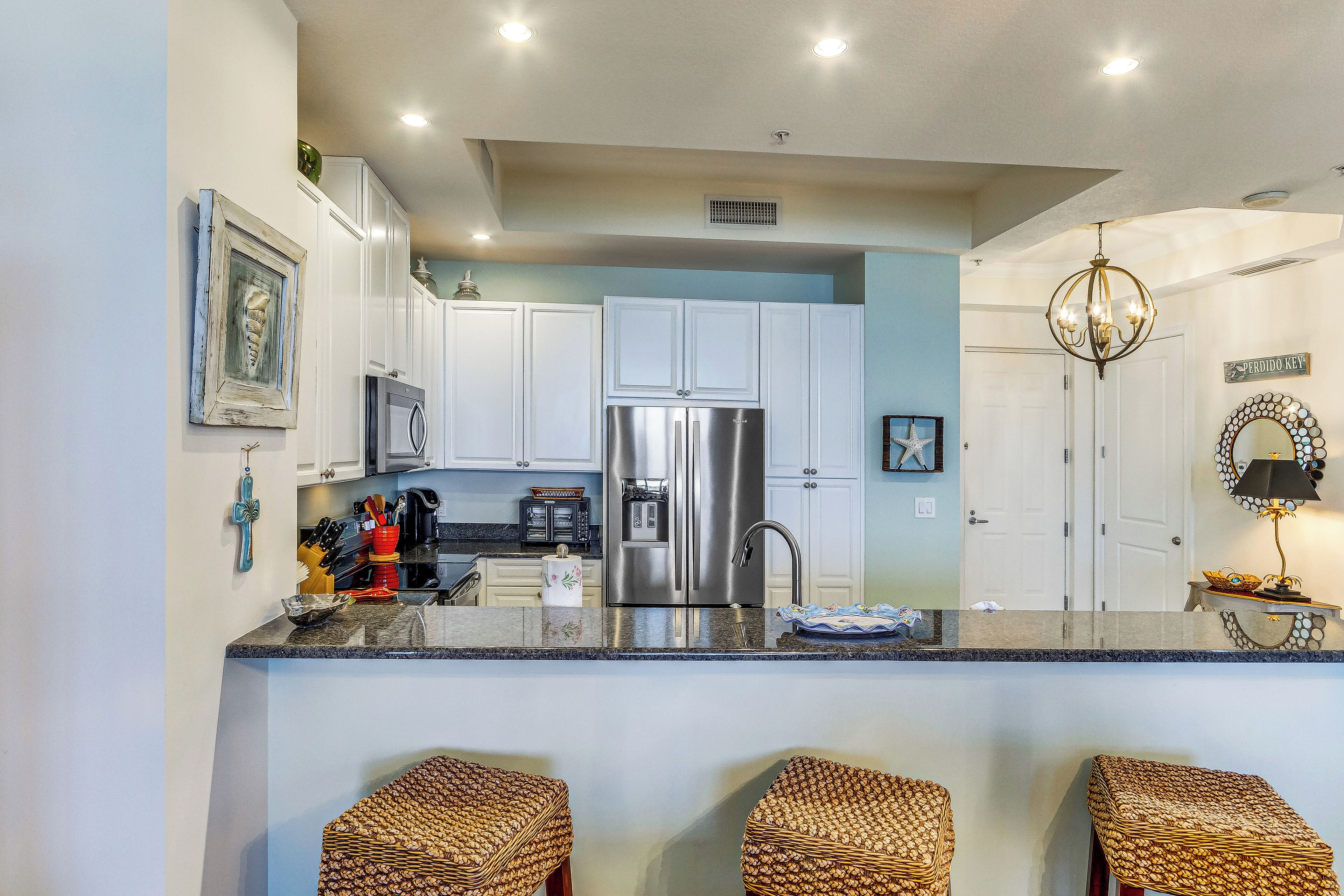 A kitchen with white cabinets, a stainless steel refrigerator, and a central island with bar stools.