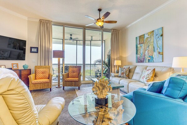A spacious living room with a large glass coffee table, a blue sofa, and a wicker armchair.