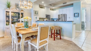 A dining area with a wooden table, white chairs, and a chandelier. - Perdido Key Beach Condo w/ Community Perks! (Pensacola)