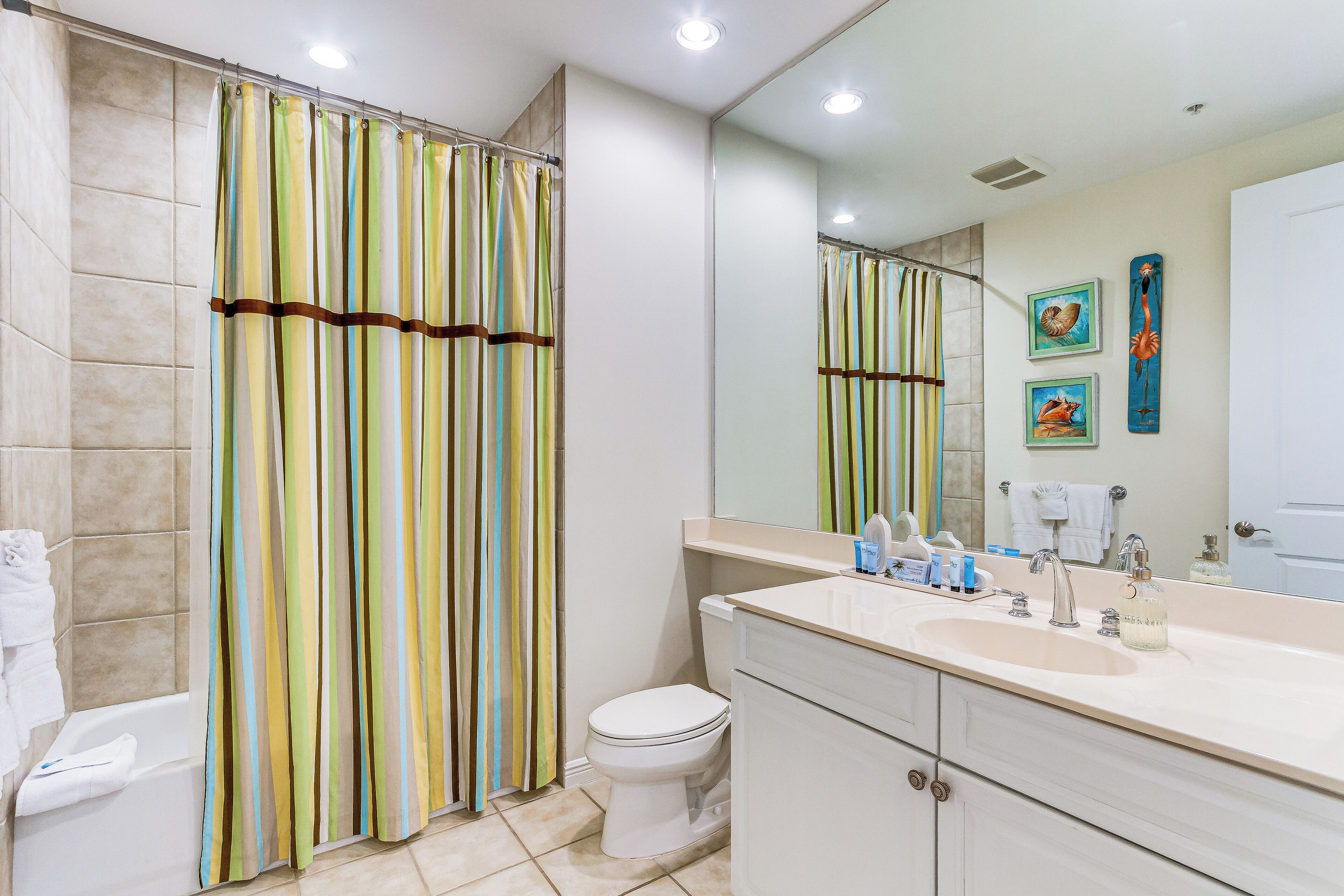 A bathroom with a shower curtain, toilet, sink, and mirror.