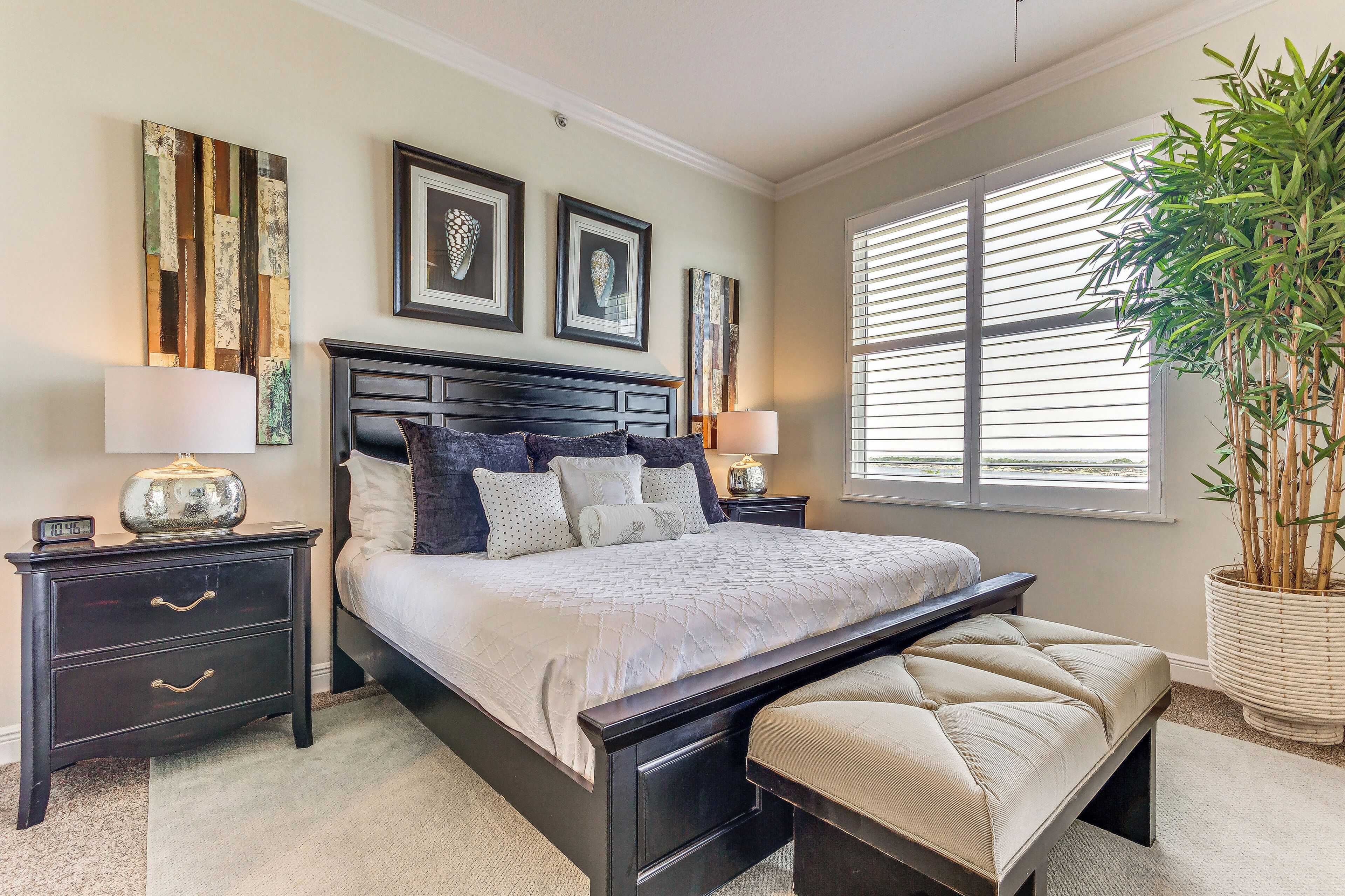 A bedroom with a large bed, two bedside tables, a bench, and a potted plant.