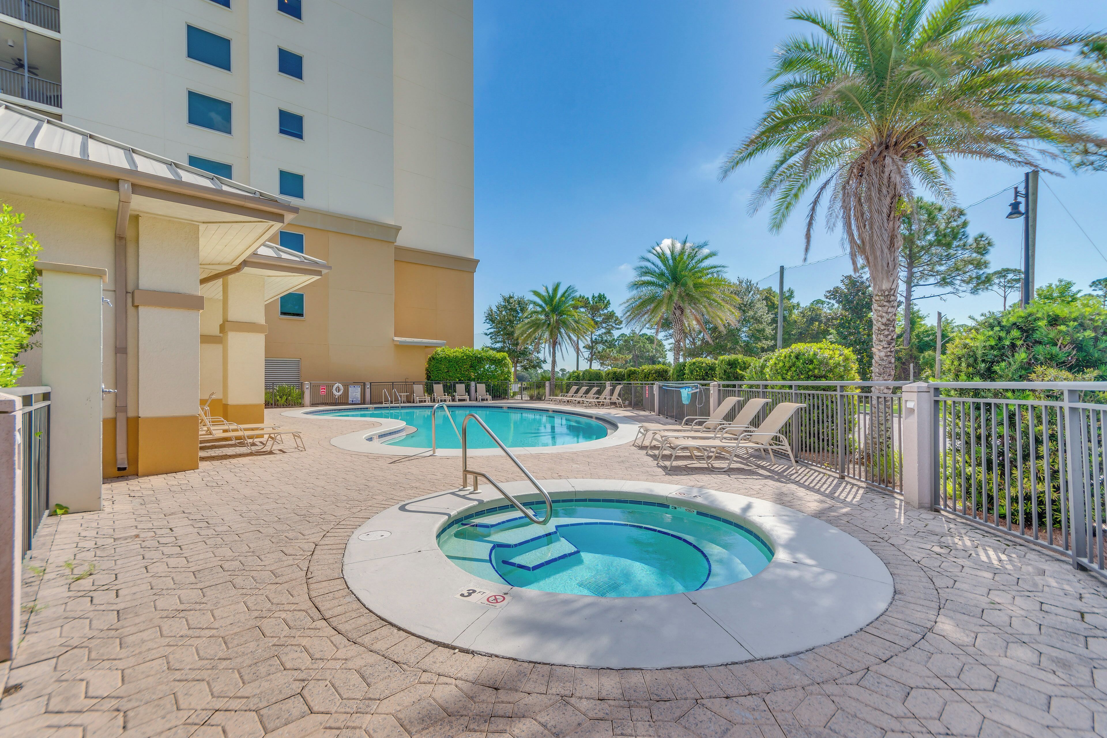 Un área de piscina con dos jacuzzis, una palmera y un edificio con balcones.