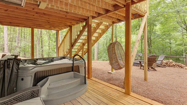 A wooden deck with a hot tub, wicker chair, and a staircase leading to an upper level. - Family-friendly Dadeville Cabin w/ Hot Tub & Porch (Dadeville)