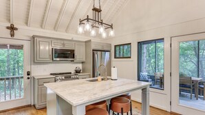 A modern kitchen with a marble island, stainless steel appliances, and a large window overlooking a deck. - Family-friendly Dadeville Cabin w/ Hot Tub & Porch (Dadeville)