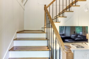 Una escalera de madera con escalones y barandilla, que conduce a una plataforma con pared blanca y ventana.