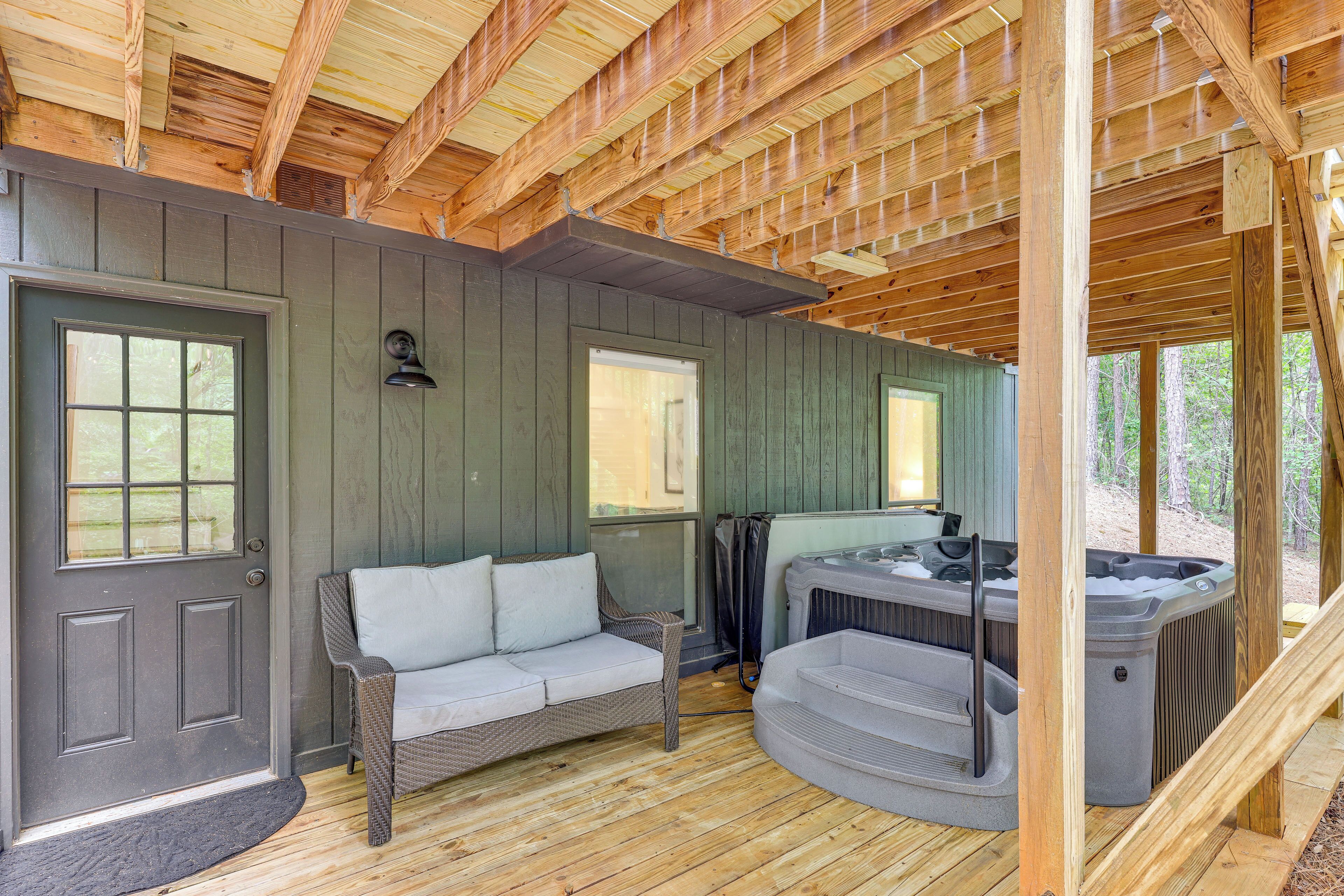 A wooden deck with a gray door, a wicker sofa, and a hot tub.