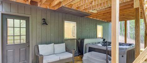 A wooden deck with a gray door, a wicker sofa, and a hot tub.