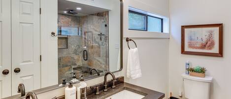 A bathroom with a large mirror, a sink with a granite countertop, a toilet, and a window above the sink.