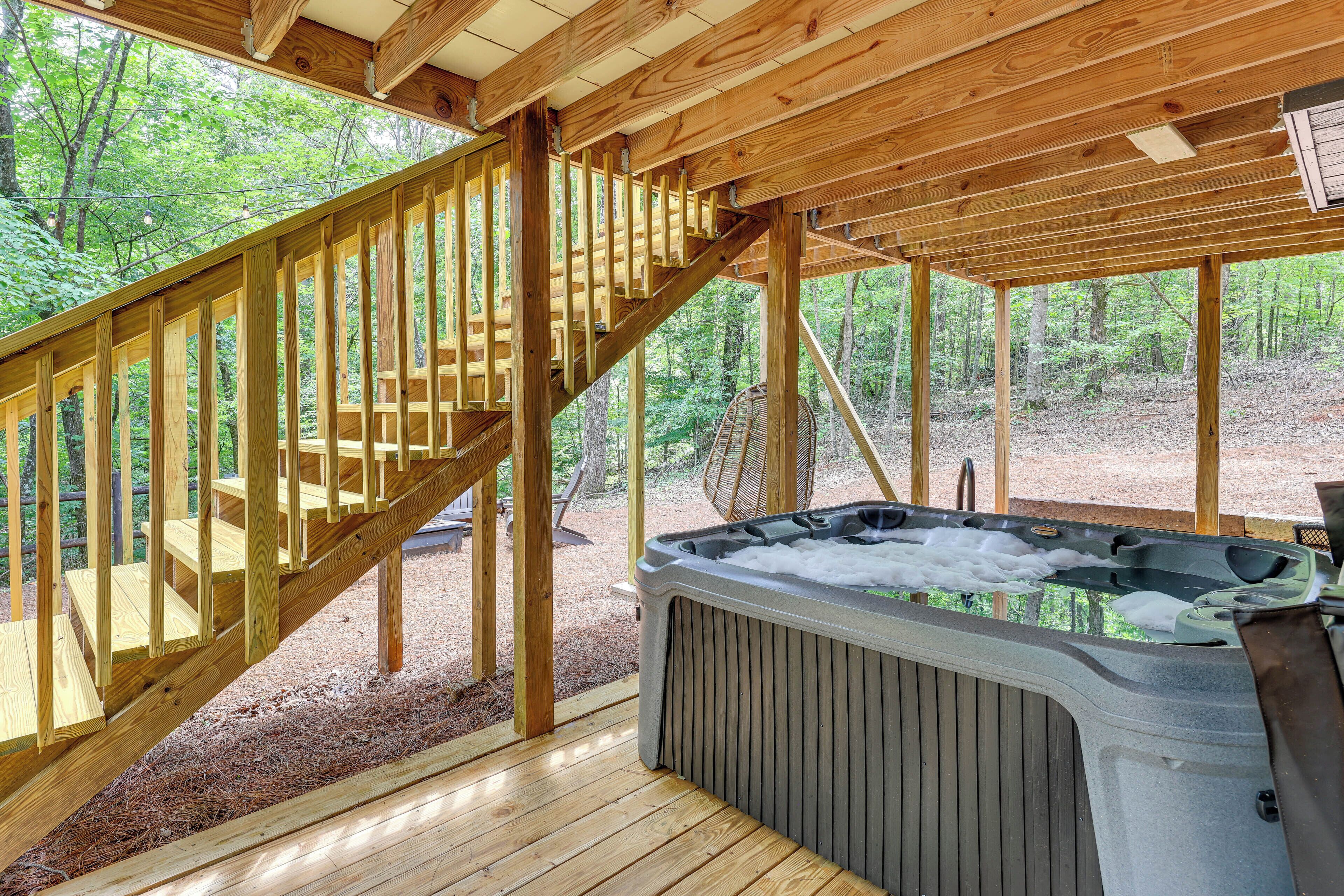 Une terrasse en bois avec un jacuzzi, un escalier en bois et une vue sur la forêt.