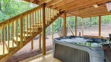A wooden deck with a hot tub, wooden stairs, and a view of the forest.
