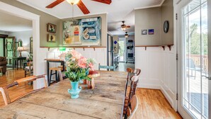 Un coin repas avec une table en bois, des chaises, un vase de fleurs, des ventilateurs de plafond et des œuvres d’art accrochées aux murs.