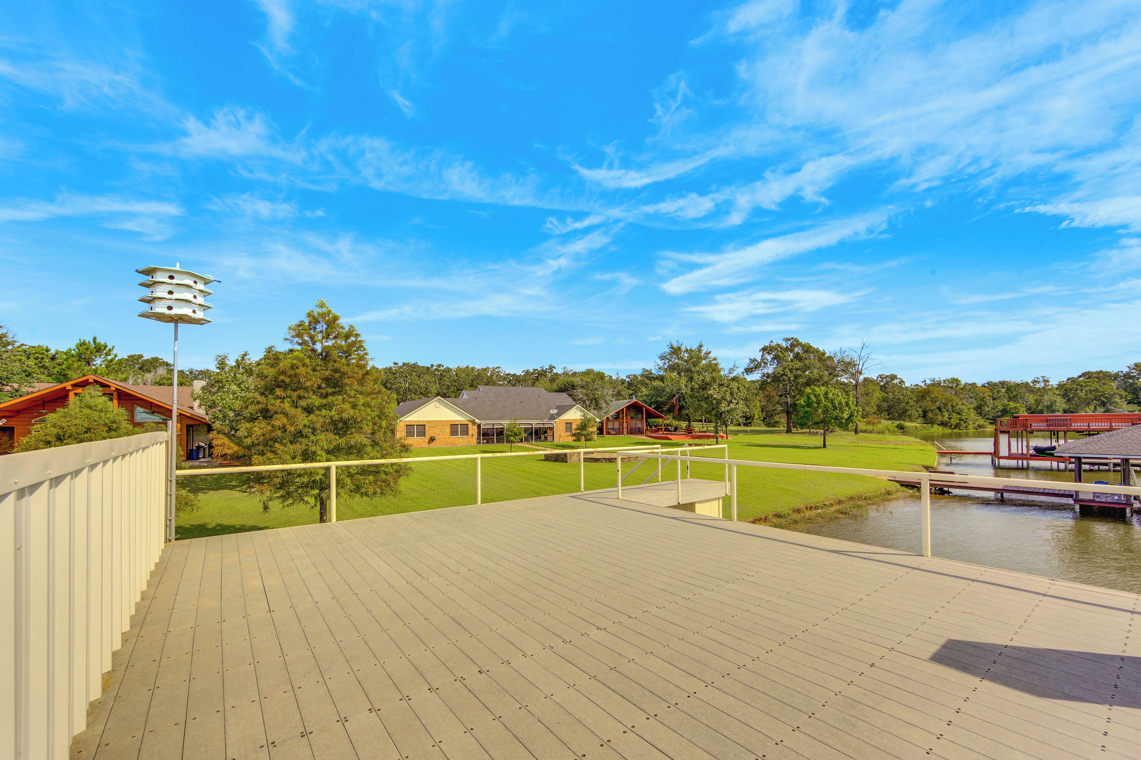 A wooden deck with a railing overlooking a body of water, a gazebo, and houses in the background.