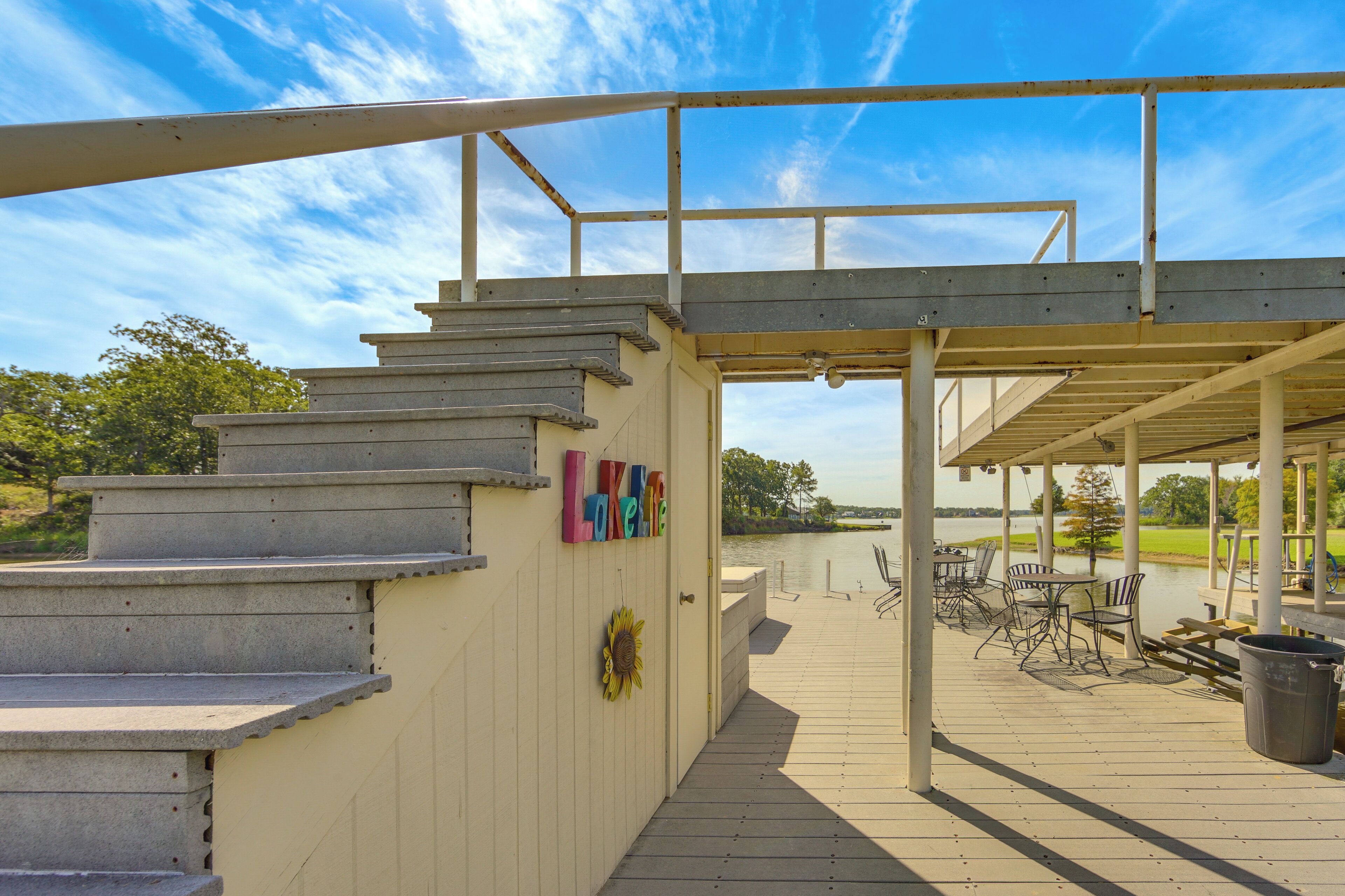 Una terraza cubierta al aire libre con escalones que conducen a un espacio resguardado, mobiliario exterior y vistas a una masa de agua.