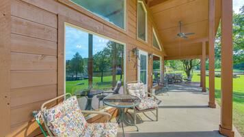 An outdoor patio with wooden walls, large windows, and a ceiling fan.