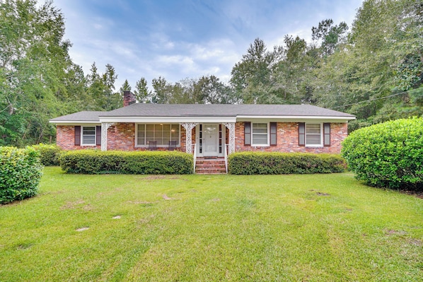 A two-story brick house with a front porch, surrounded by well-maintained hedges and a grassy lawn.
