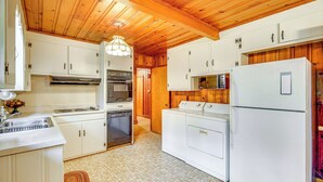 Una cocina con techo de madera, armarios blancos, electrodomésticos de acero inoxidable y un microondas.