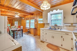 A kitchen with wooden cabinets, a white countertop, and a window with a view of greenery.