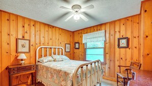 Un dormitorio con paneles de madera, una cama con colcha floral, una mesita de noche, una silla y un escritorio.