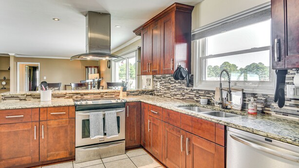 A modern kitchen with wooden cabinets, granite countertops, stainless steel appliances, and a large window providing natural light. - Luxe Lakefront Portsmouth Home: Fish, Swim & Play! (Portsmouth)
