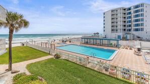 Une piscine avec vue sur l’océan, une terrasse délimitée par une clôture et un immeuble à plusieurs étages doté de balcons.