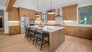Eine moderne Küche mit Holzausbau, einer großen Kochinsel mit Barhocker, Edelstahlgeräten und Pendelleuchten.