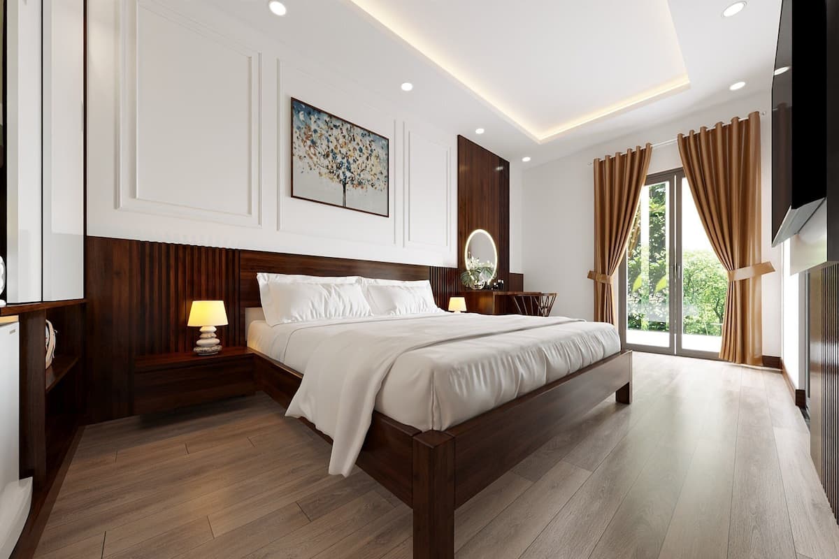 A modern bedroom with a large bed, wooden headboard, bedside tables with lamps, a large window with curtains, and a wall-mounted TV.