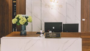Un mostrador de recepción de hotel con encimera de mármol, un jarrón de flores y un cartel que indica la zona de recepción.