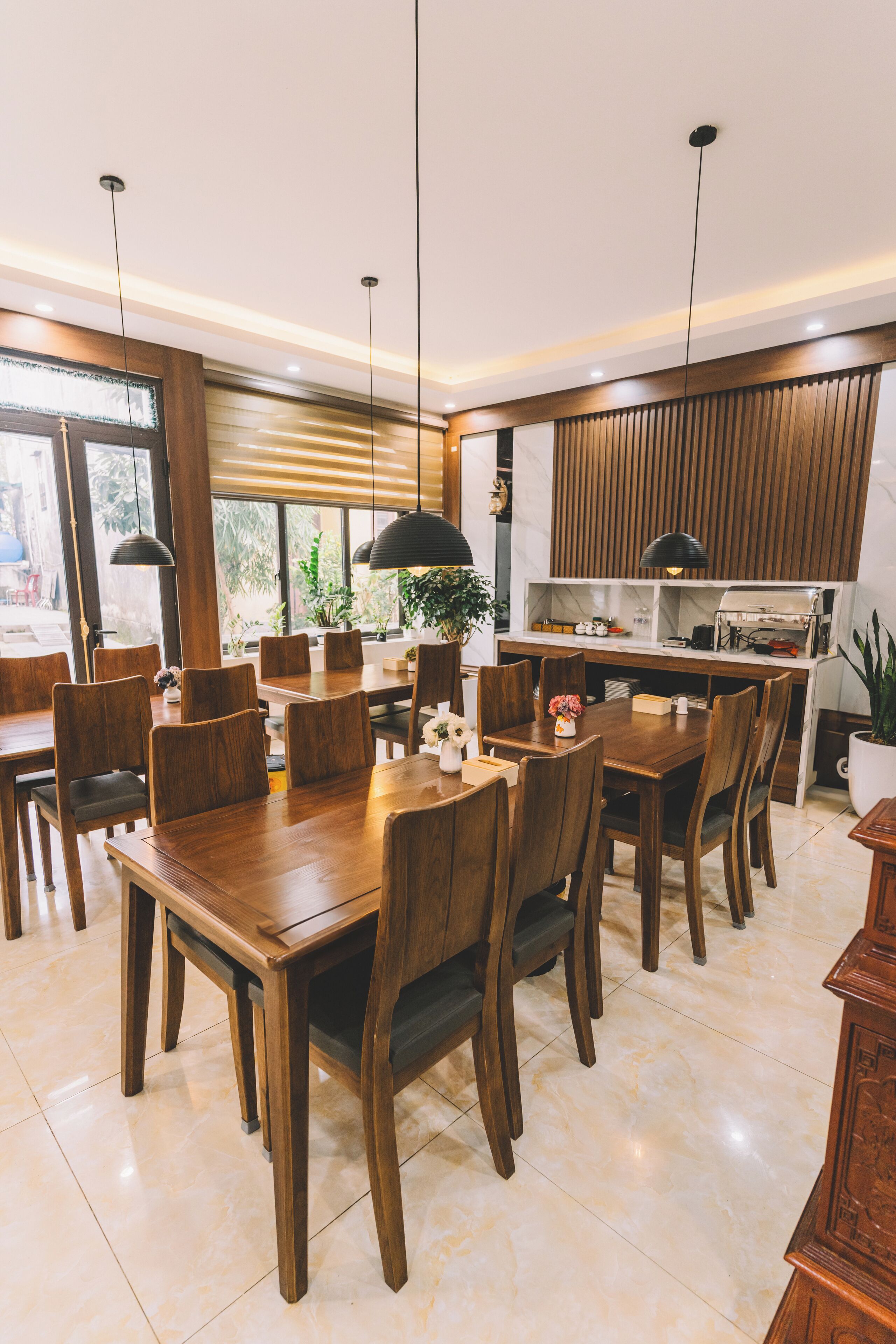A modern dining area with wooden tables and chairs, pendant lighting, and a kitchen area with wooden cabinets and appliances.
