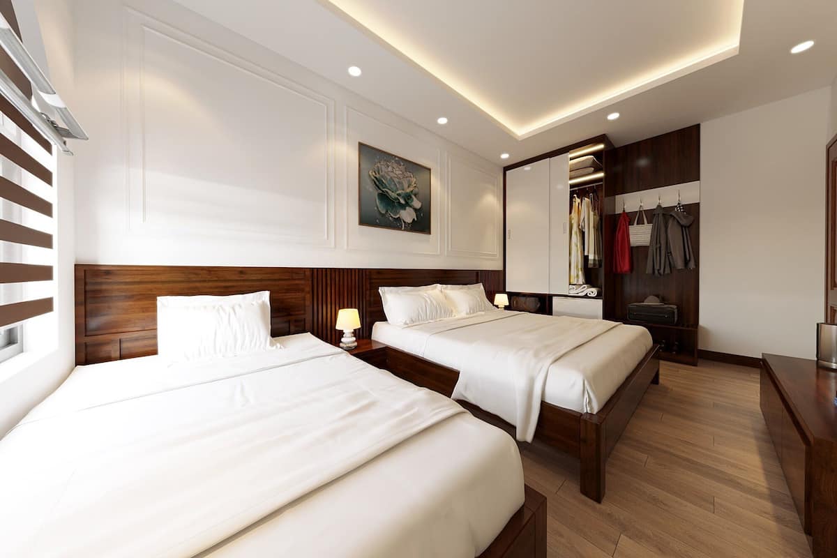 A hotel room with two beds, a wooden headboard, a painting on the wall, a wardrobe, and a mirror.