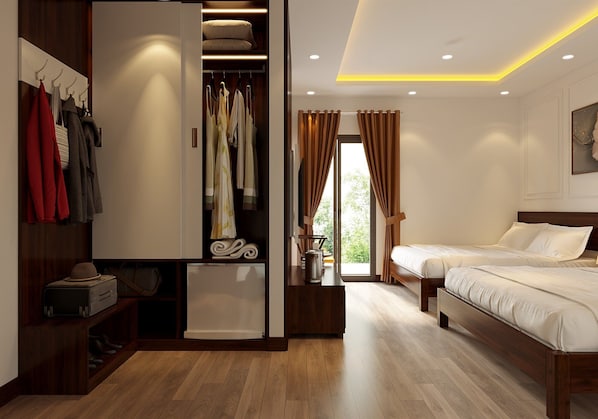 A hotel room with a wooden floor, a wardrobe with hanging clothes, a bed, and a small table with a kettle.