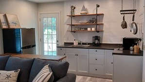 A modern kitchen with white cabinets, a grey sofa, and a dining area. - Charming 1-bedroom cottage in lovely Pawleys Island Walk to Boat ramp Dogs ok (Pawleys Island)