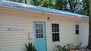 A small, single-story building with a turquoise door and a sign reading "The Bella." - Charming 1-bedroom cottage in lovely Pawleys Island Walk to Boat ramp Dogs ok (Pawleys Island)