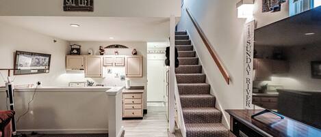 A modern kitchen with a central island, a dining area with a wooden table, and a staircase leading to a second floor.