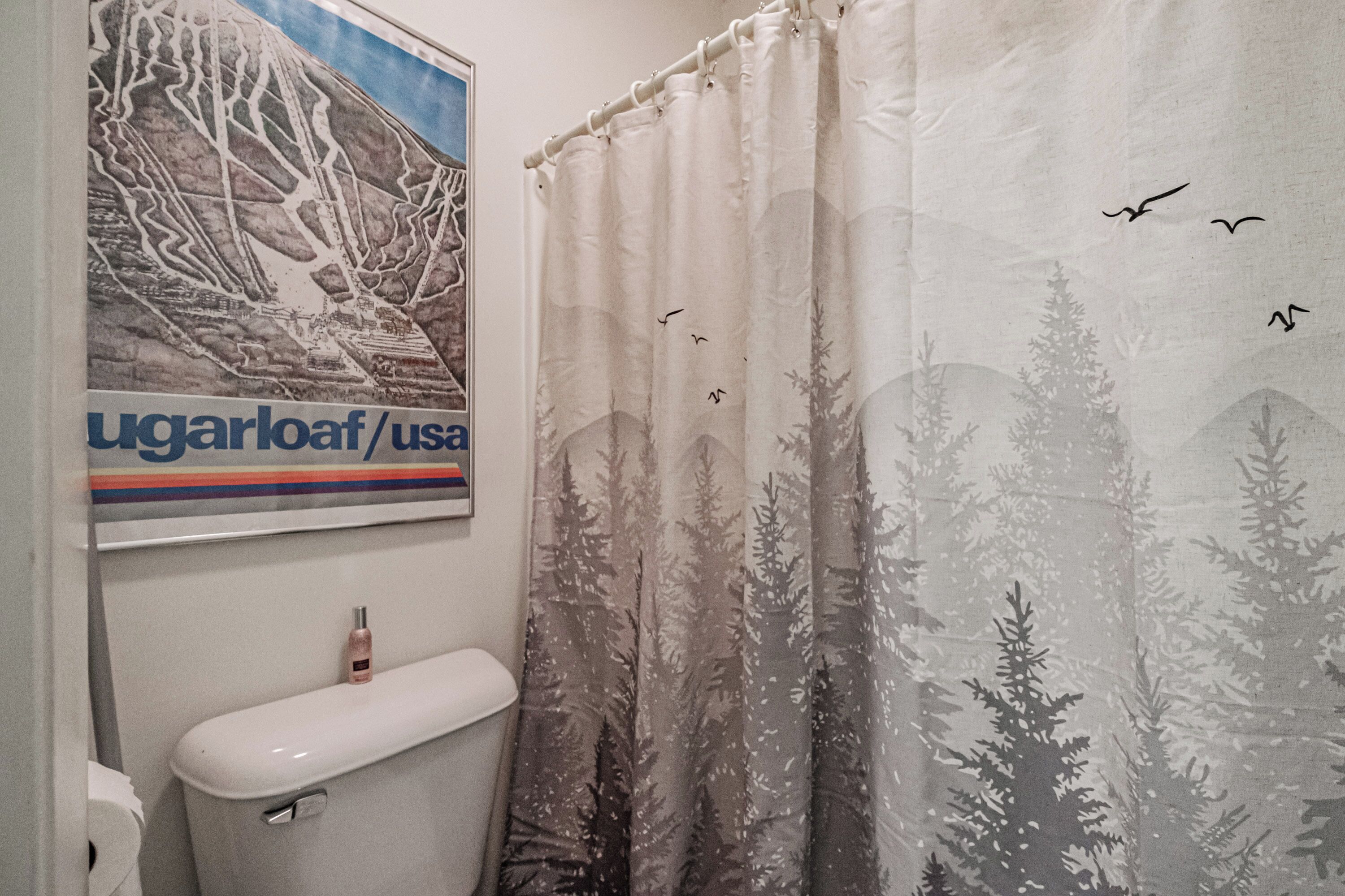 Un baño con inodoro, un cartel y una cortina de ducha con diseño de bosque y pájaros.