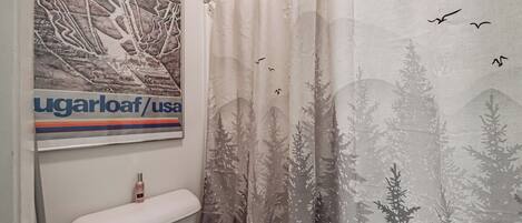 Un baño con inodoro, un cartel y una cortina de ducha con diseño de bosque y pájaros.