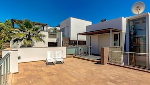 A modern outdoor patio with a pool, white lounge chairs, and a covered seating area.