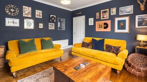 Ein Wohnzimmer mit zwei gelben Sofas, einem Holztisch und verschiedenen gerahmten Bildern an den Wänden.