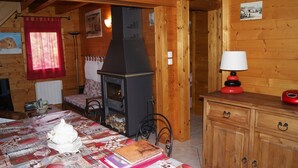 Een gezellig interieur van een blokhut met een open haard, houten wanden, een eettafel met een quilt en een klein kastje met lades.