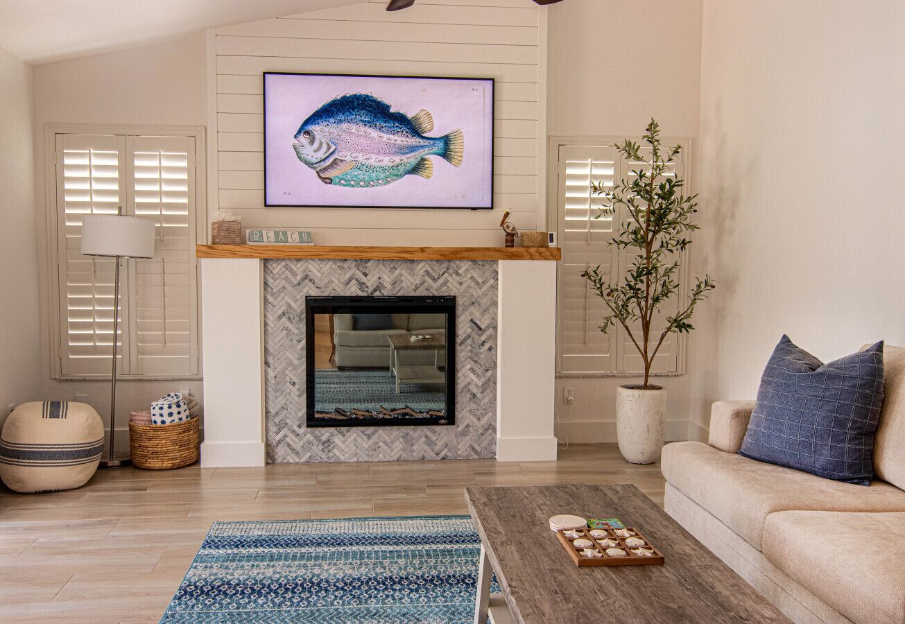 A living room with a fireplace, a sofa, a coffee table, a TV mounted above the fireplace, and a potted plant.