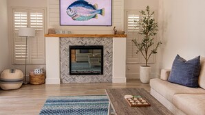 Una sala de estar con chimenea, un sofá, una mesa de centro, un televisor sobre la chimenea y una planta en maceta.