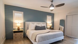 Un dormitorio con cama, dos mesitas de noche, ventilador de techo y un espejo grande.