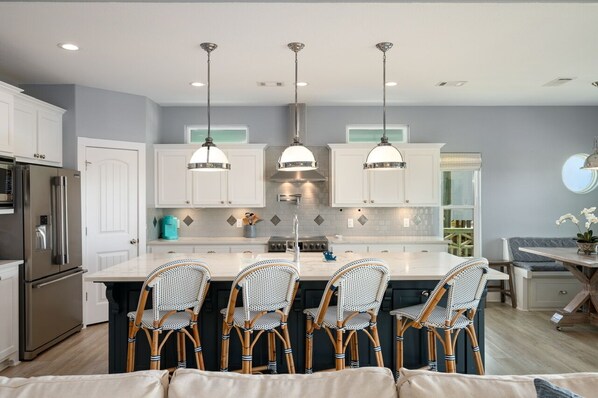 Una cocina moderna con armarios blancos, una isla central con taburetes altos e iluminación colgante.