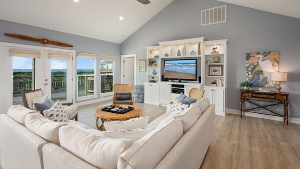 A spacious living room with a large TV, comfortable seating, and a balcony with a view.