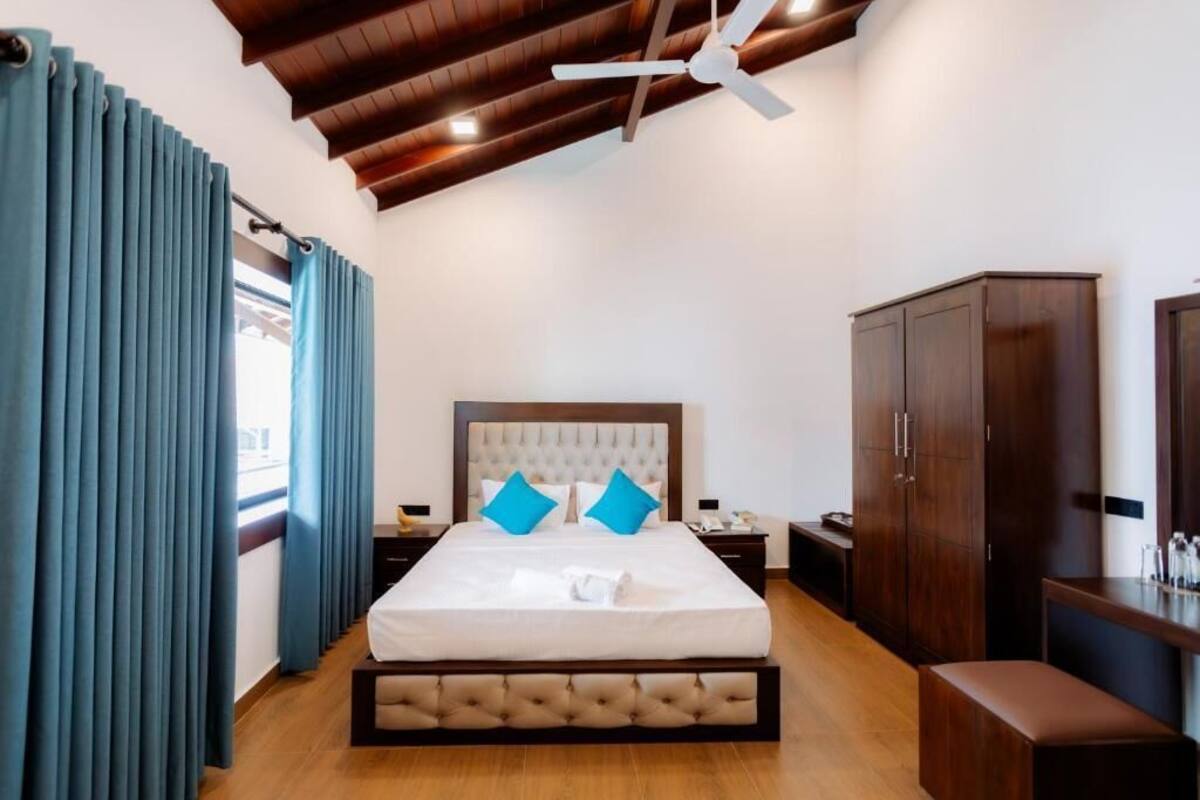 A bedroom with a large bed, wooden headboard, blue curtains, a ceiling fan, and a wooden wardrobe.