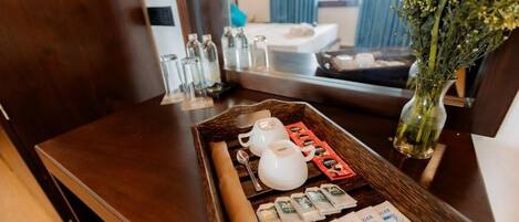 A wooden tray with a tea set, sugar packets, and a rolled towel on a hotel room table.